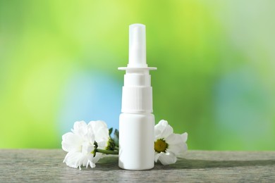 Photo of Allergy treatment. Nasal spray and flowers on wooden table against blurred background