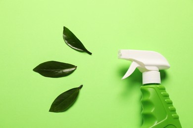 Photo of Spray bottle of cleaning product and leaves on green background, flat lay