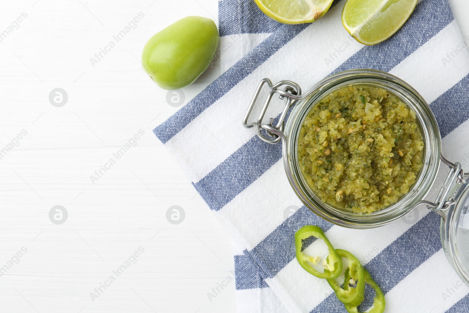 Photo of Delicious salsa sauce in jar, lime and green chili pepper on white wooden table, flat lay. Space for text