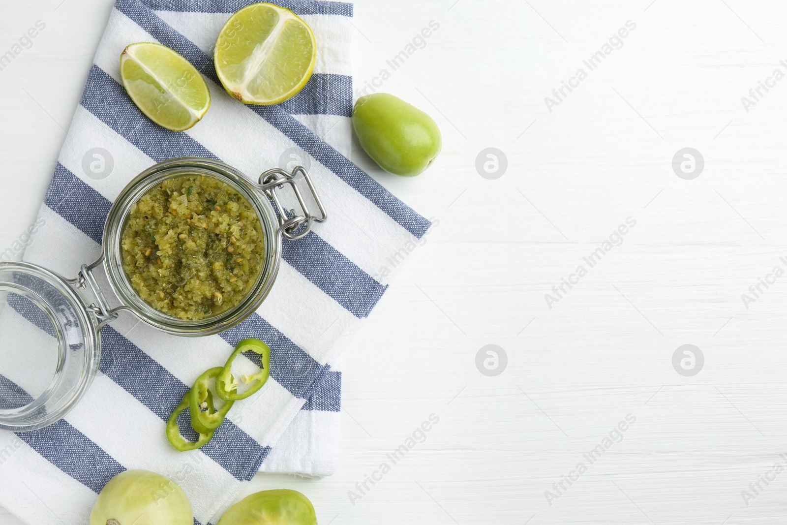 Photo of Delicious salsa sauce in jar, lime and green chili pepper on white wooden table, flat lay. Space for text