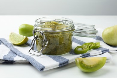 Photo of Delicious salsa sauce in jar and products on white wooden table, closeup