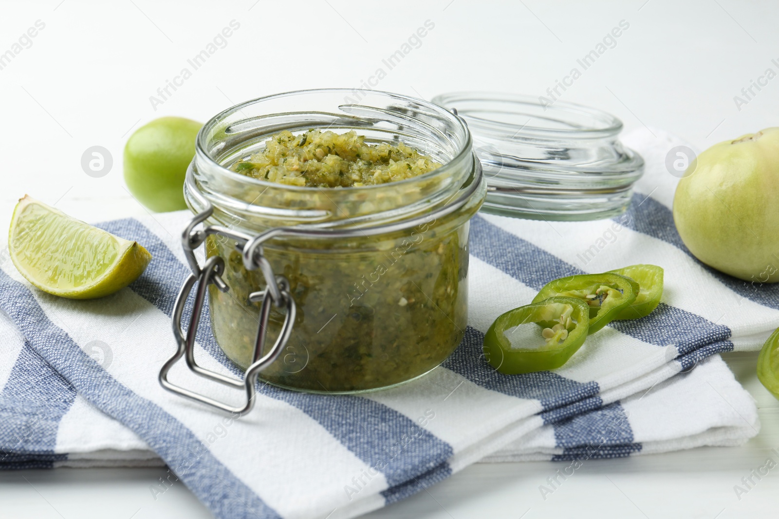 Photo of Delicious salsa sauce in jar and products on white wooden table, closeup