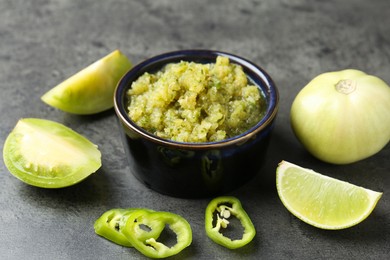 Photo of Delicious salsa sauce in bowl and products on grey textured table, closeup