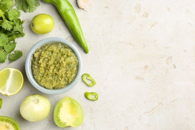 Photo of Delicious salsa sauce in bowl and ingredients on light textured table, flat lay. Space for text