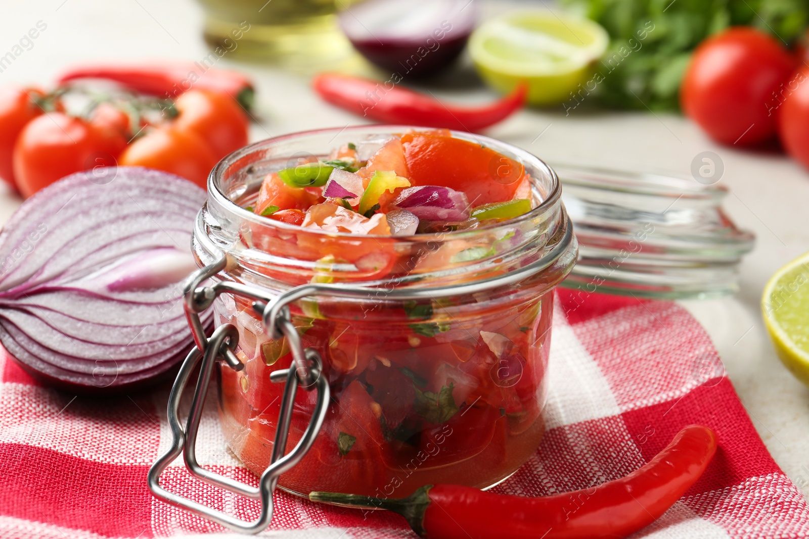 Photo of Delicious salsa (Pico de gallo) in jar and ingredients on light table, closeup