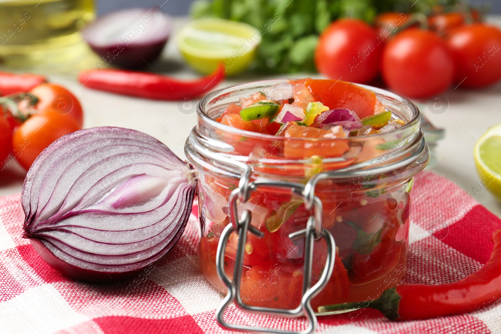 Photo of Delicious salsa (Pico de gallo) in jar and ingredients on light table, closeup