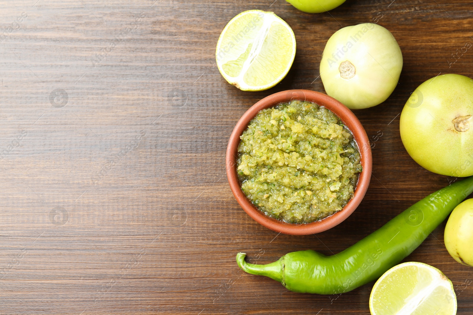 Photo of Delicious salsa sauce in bowl and products on wooden table, flat lay. Space for text