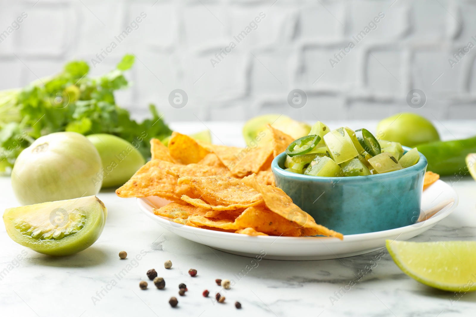 Photo of Delicious salsa with nachos on white marble table, closeup