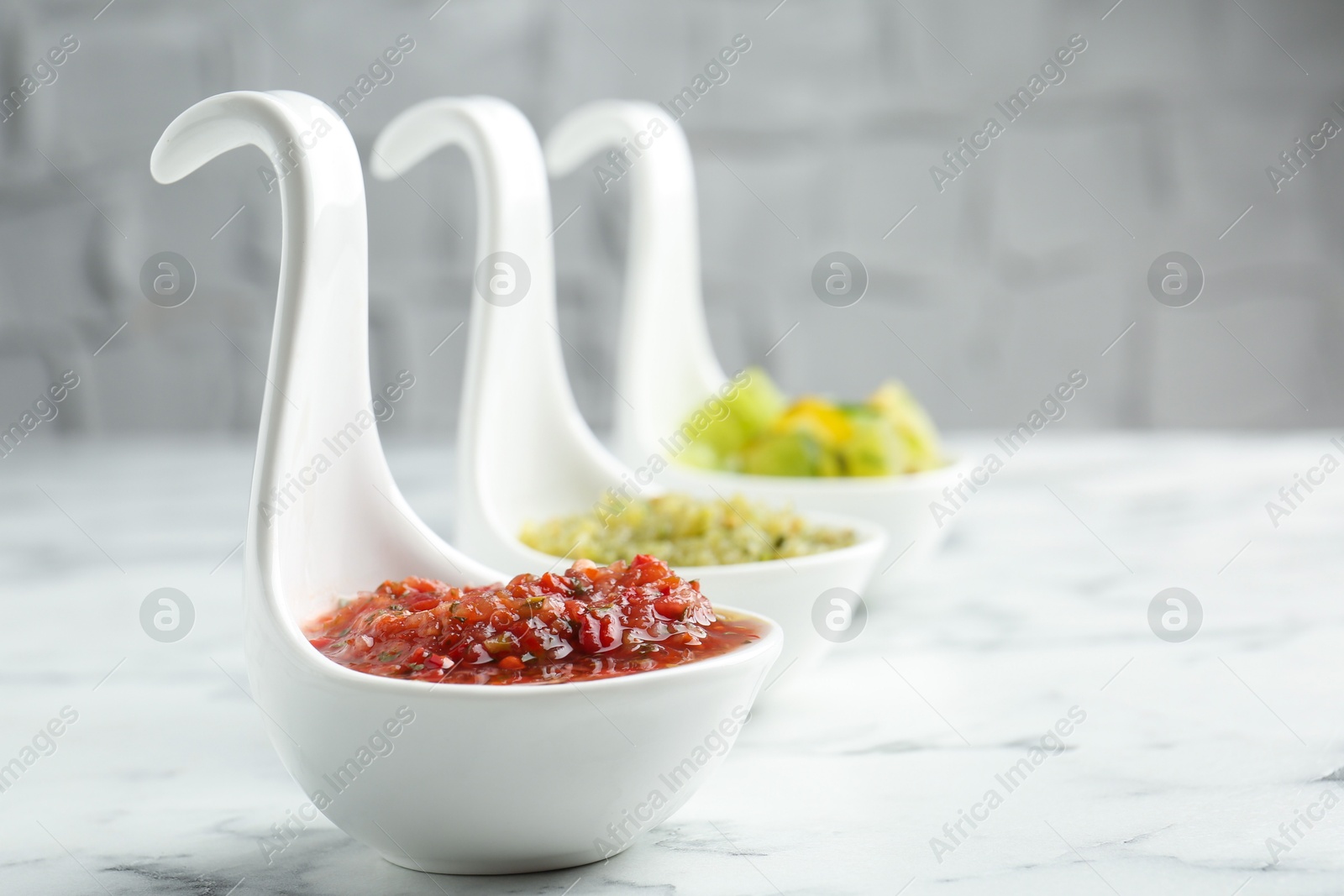 Photo of Sauce boats with salsa on white marble table, selective focus