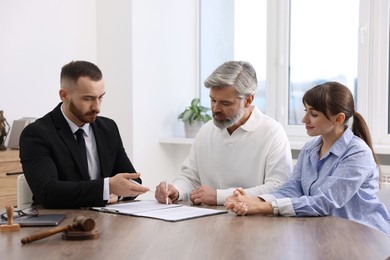 Photo of Clients signing notarial paperwork during meeting with lawyer at wooden desk indoors