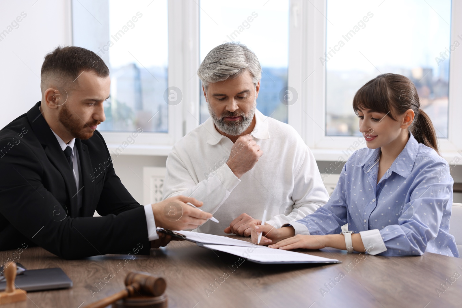 Photo of Clients signing notarial paperwork during meeting with lawyer at wooden desk indoors