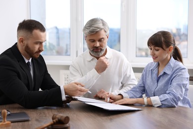 Clients signing notarial paperwork during meeting with lawyer at wooden desk indoors