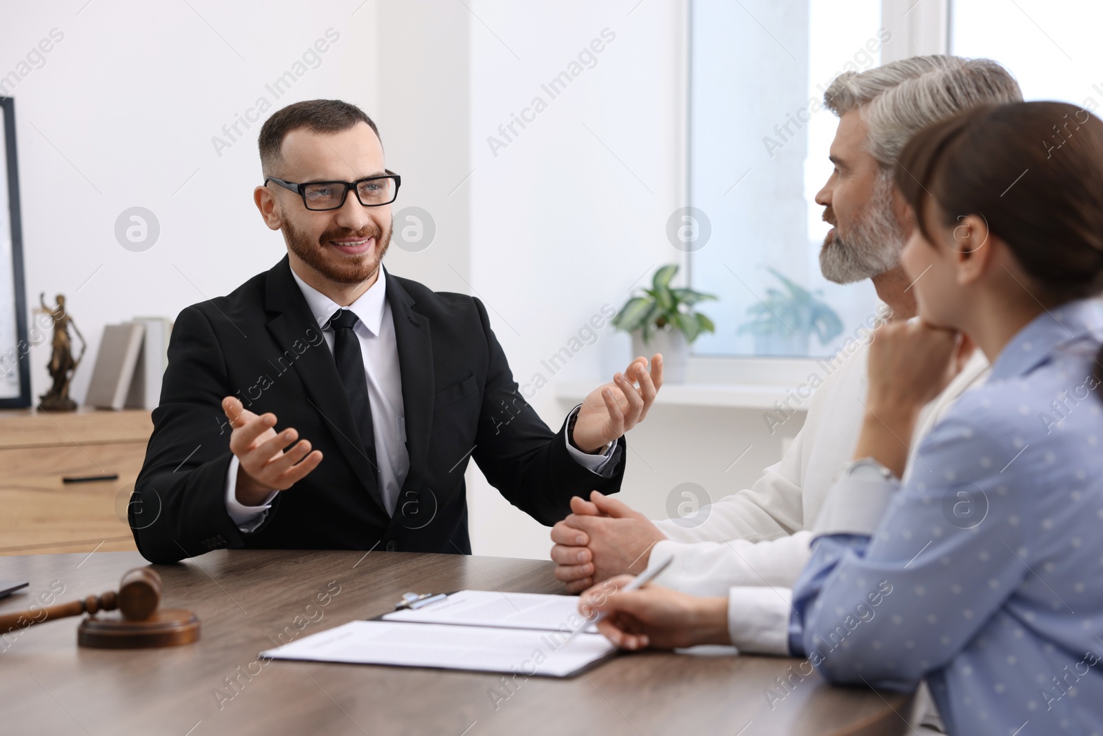 Photo of Couple having meeting with professional notary at wooden desk indoors