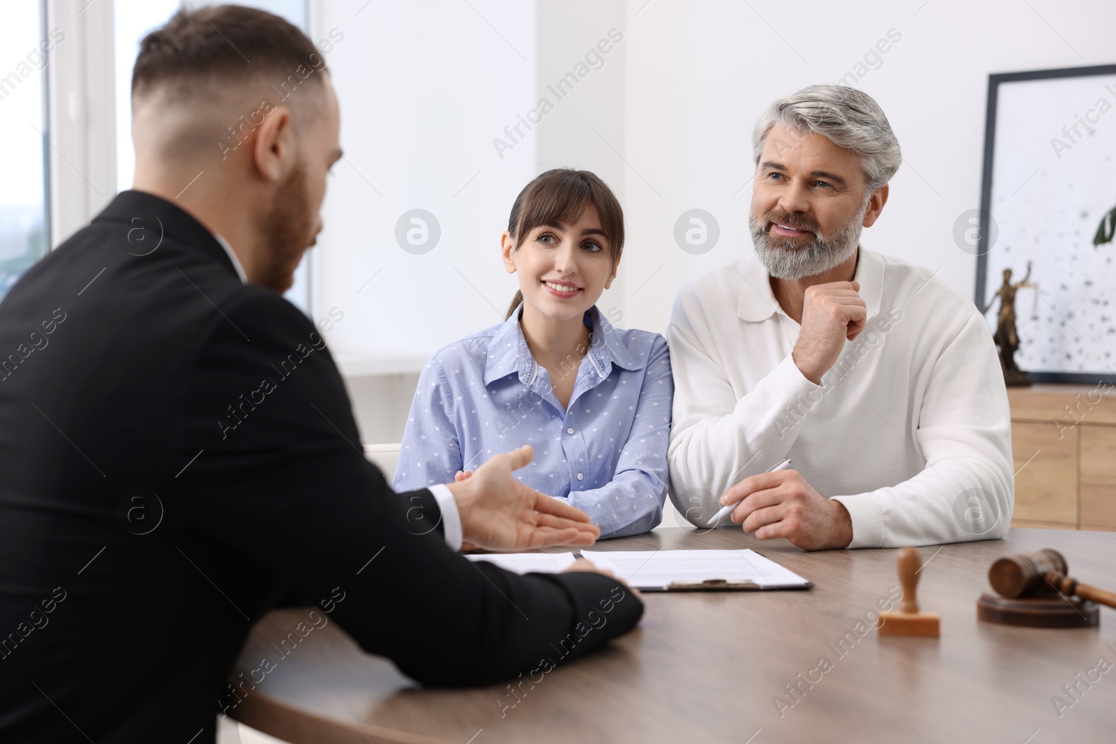 Photo of Couple having meeting with professional notary at wooden desk indoors