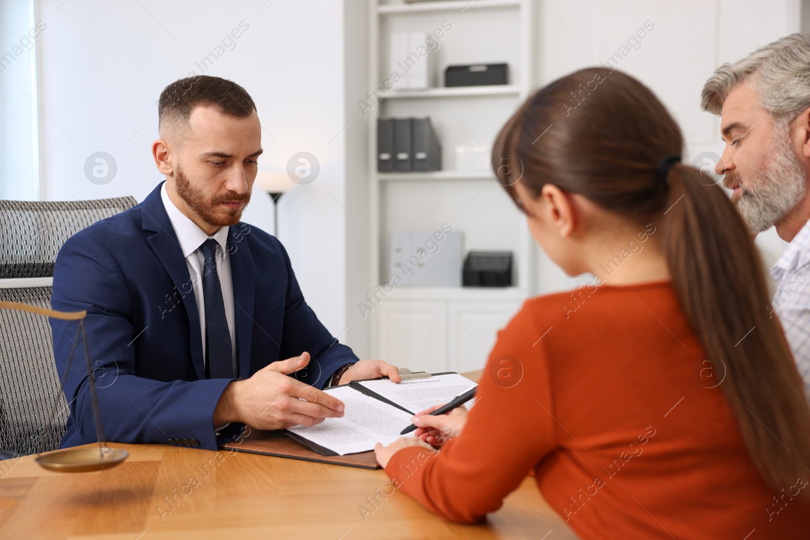 Photo of Clients signing notarial paperwork during meeting with lawyer at wooden desk indoors