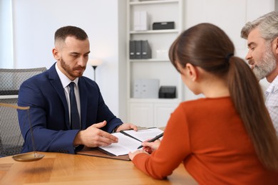 Photo of Clients signing notarial paperwork during meeting with lawyer at wooden desk indoors