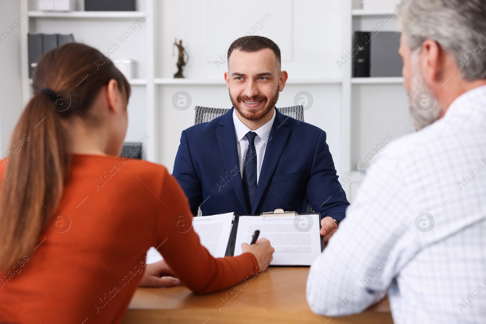 Photo of Clients signing notarial paperwork during meeting with lawyer at wooden desk indoors