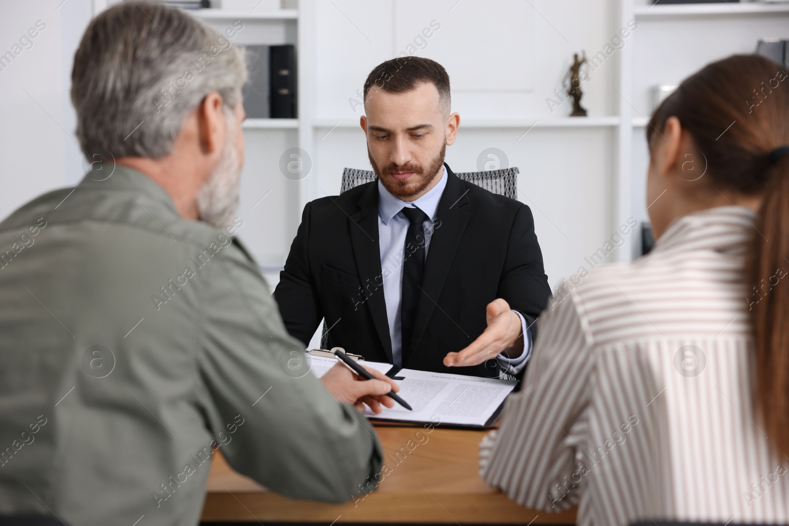 Photo of Clients signing notarial paperwork during meeting with lawyer at wooden desk indoors