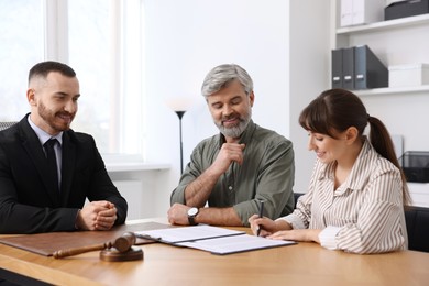 Clients signing notarial paperwork during meeting with lawyer at wooden desk indoors