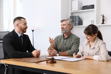 Clients signing notarial paperwork during meeting with lawyer at wooden desk indoors