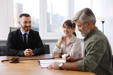 Photo of Clients signing notarial paperwork during meeting with lawyer at wooden desk indoors, selective focus