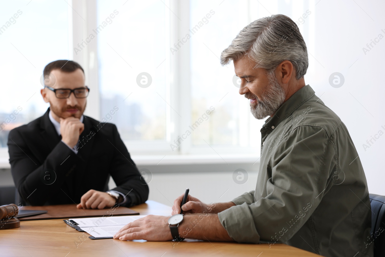 Photo of Client signing notarial paperwork during meeting with lawyer at wooden desk indoors, selective focus