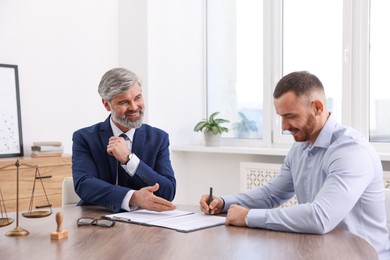 Client signing notarial paperwork during meeting with lawyer at wooden desk indoors