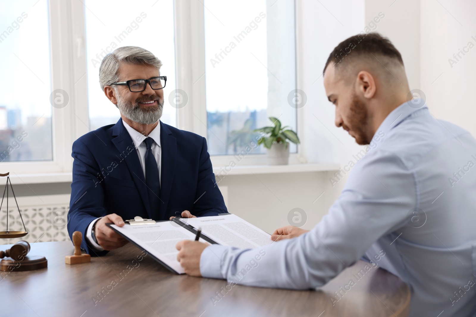 Photo of Client signing notarial paperwork during meeting with lawyer at wooden desk indoors