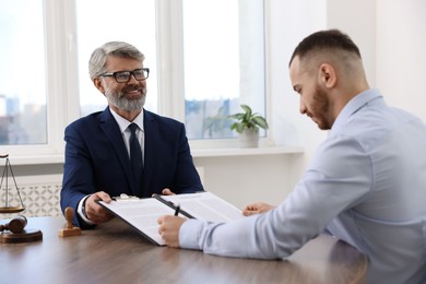 Photo of Client signing notarial paperwork during meeting with lawyer at wooden desk indoors