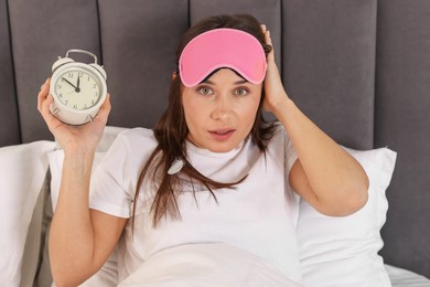 Overslept woman with alarm clock in bed at home