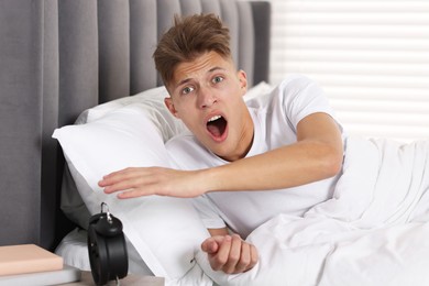 Photo of Overslept man with alarm clock in bed at home