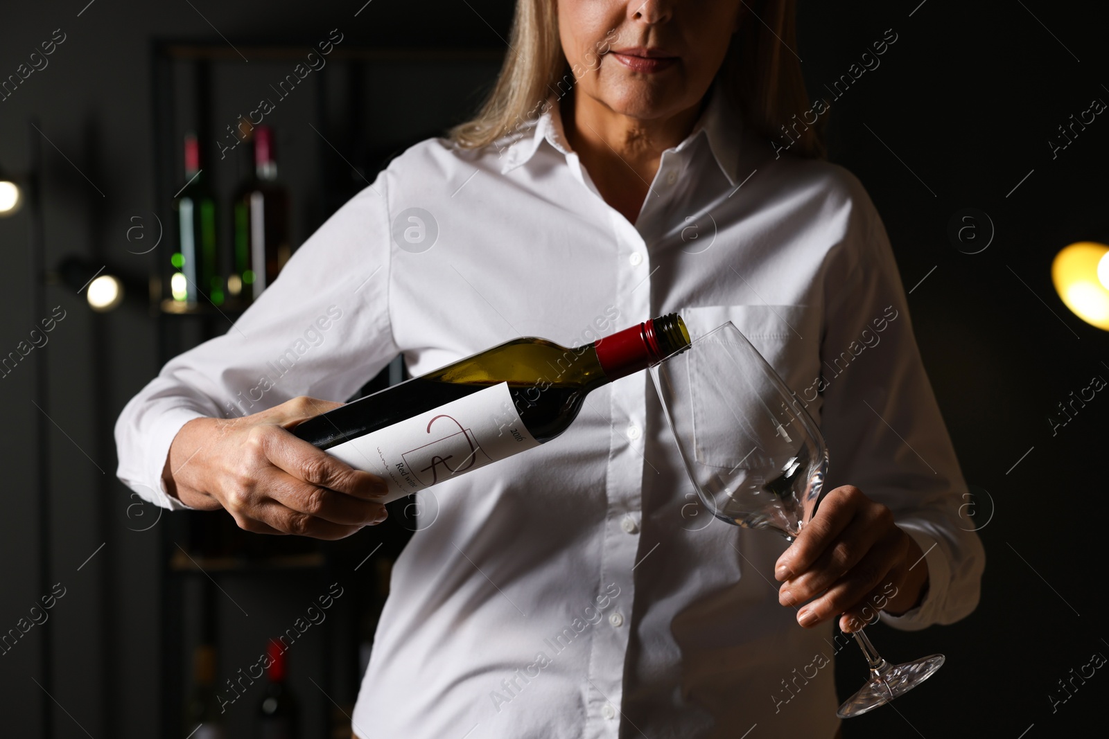 Photo of Professional sommelier pouring red wine into glass indoors, closeup