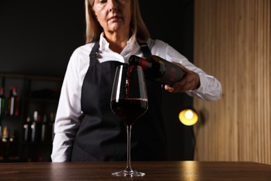 Photo of Professional sommelier pouring red wine into glass at wooden table indoors, selective focus