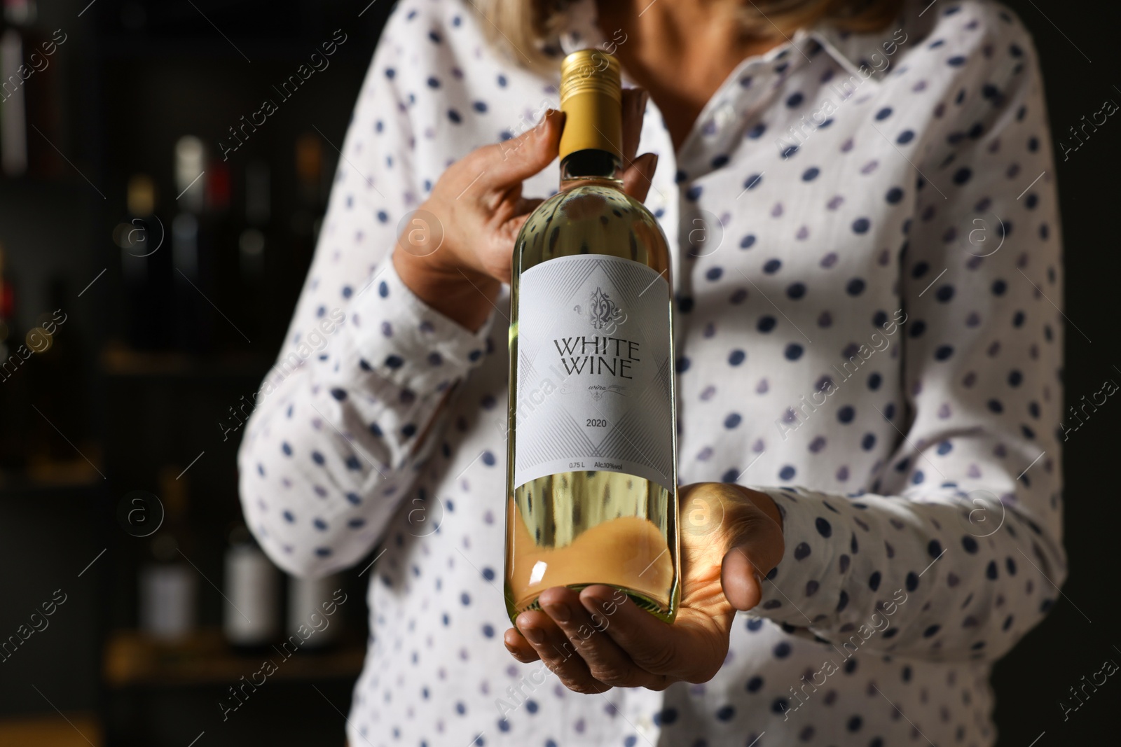 Photo of Professional sommelier holding bottle of white wine indoors, closeup