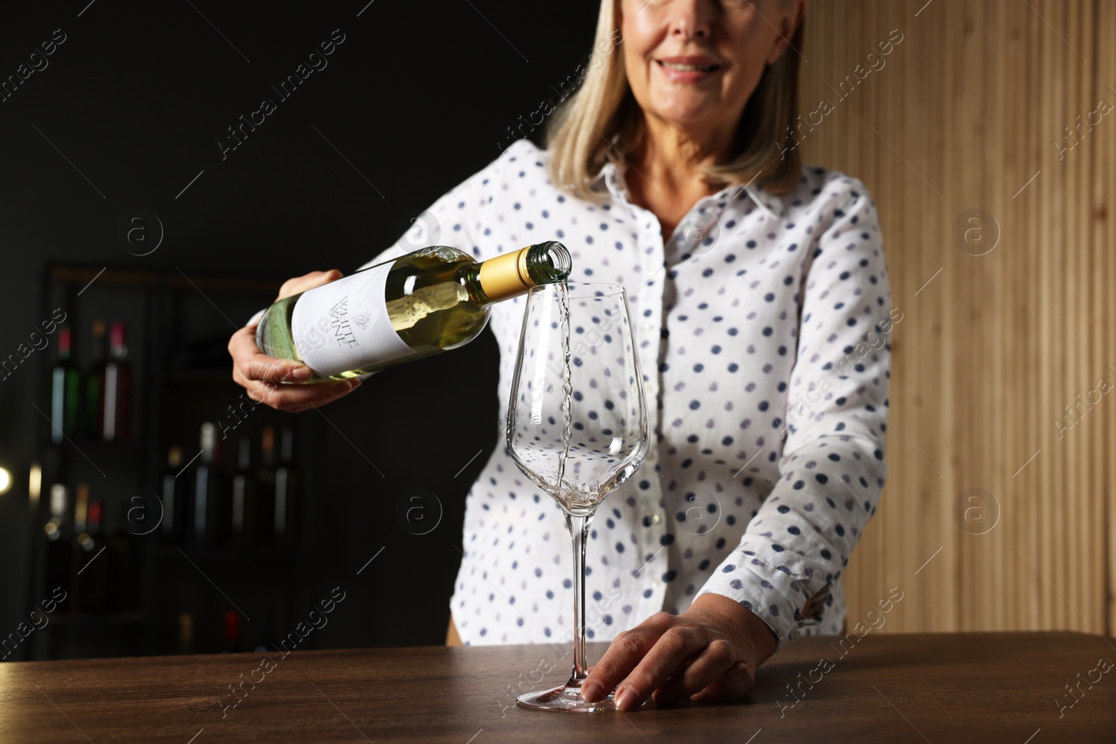 Photo of Professional sommelier pouring white wine into glass at wooden table indoors, closeup