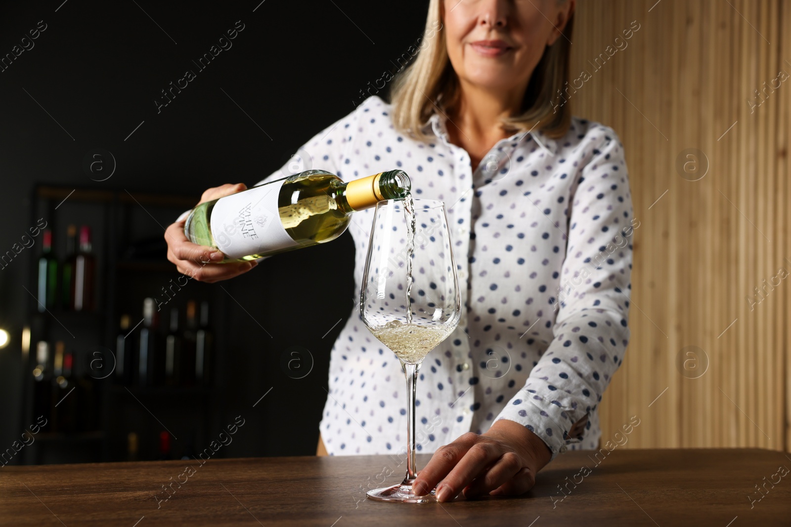 Photo of Professional sommelier pouring white wine into glass at wooden table indoors, closeup