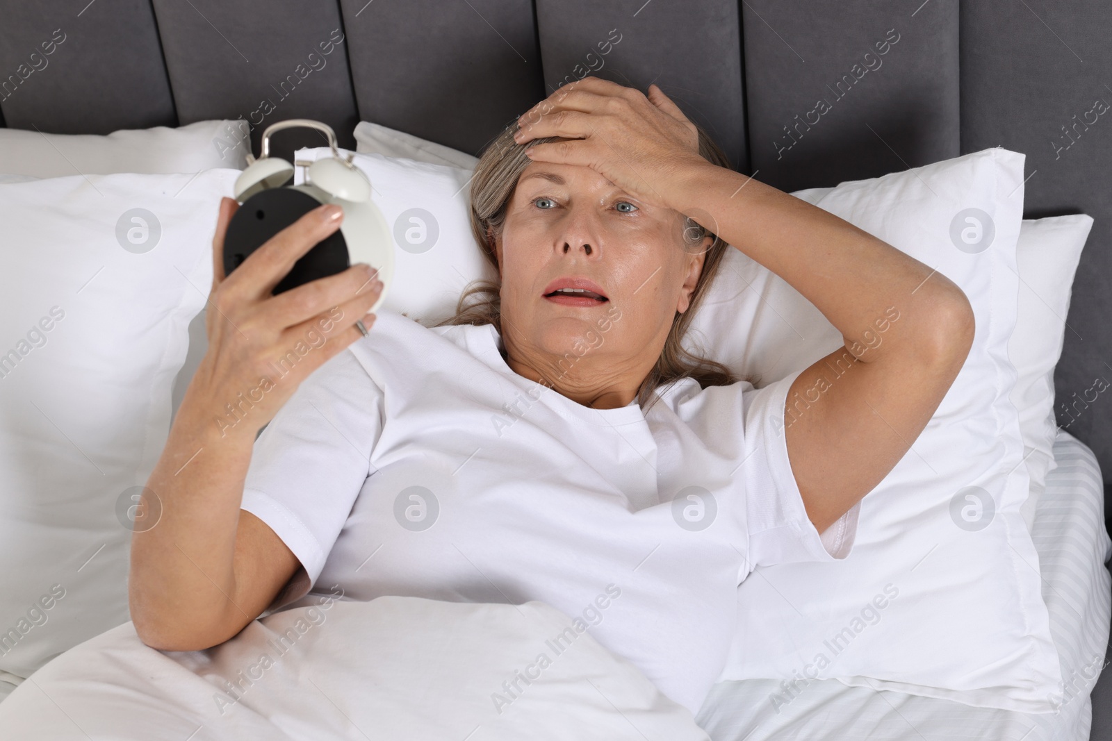 Photo of Overslept woman with alarm clock in bed at home