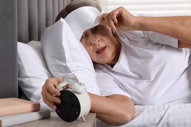 Photo of Overslept woman looking at alarm clock in bed indoors