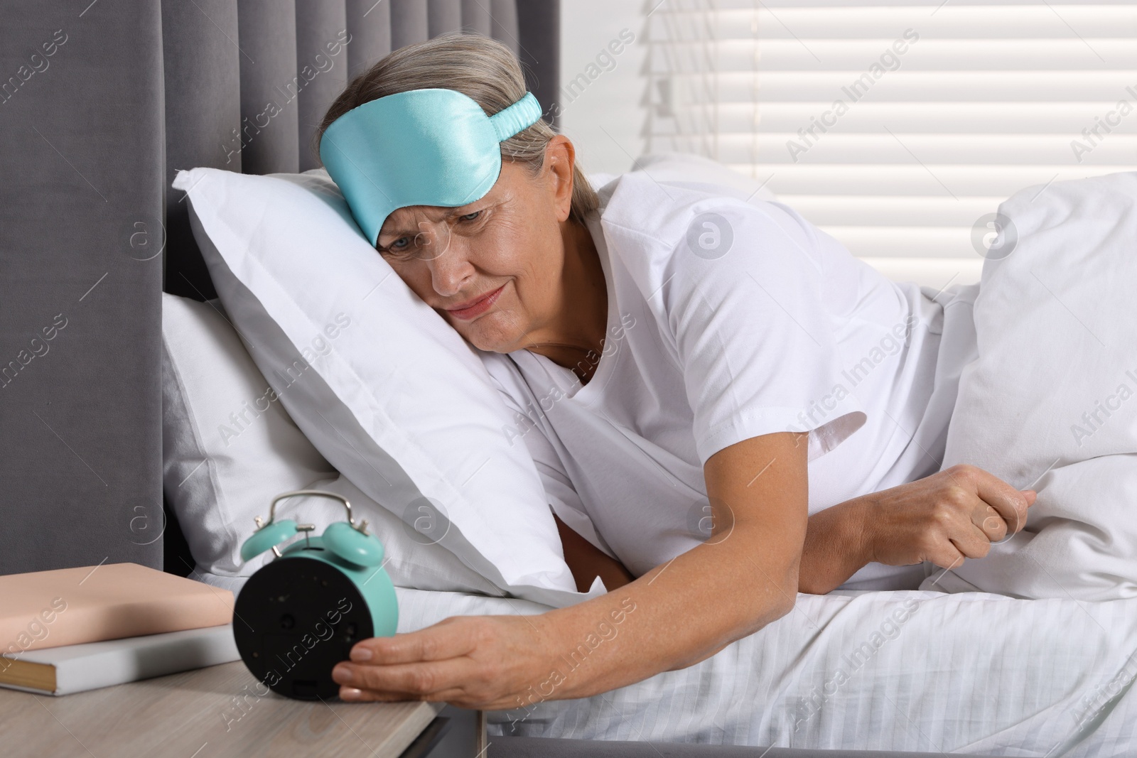 Photo of Overslept woman looking at alarm clock in bed indoors