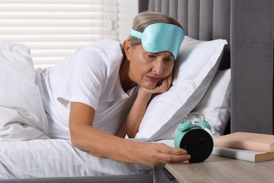 Photo of Overslept woman looking at alarm clock in bed indoors