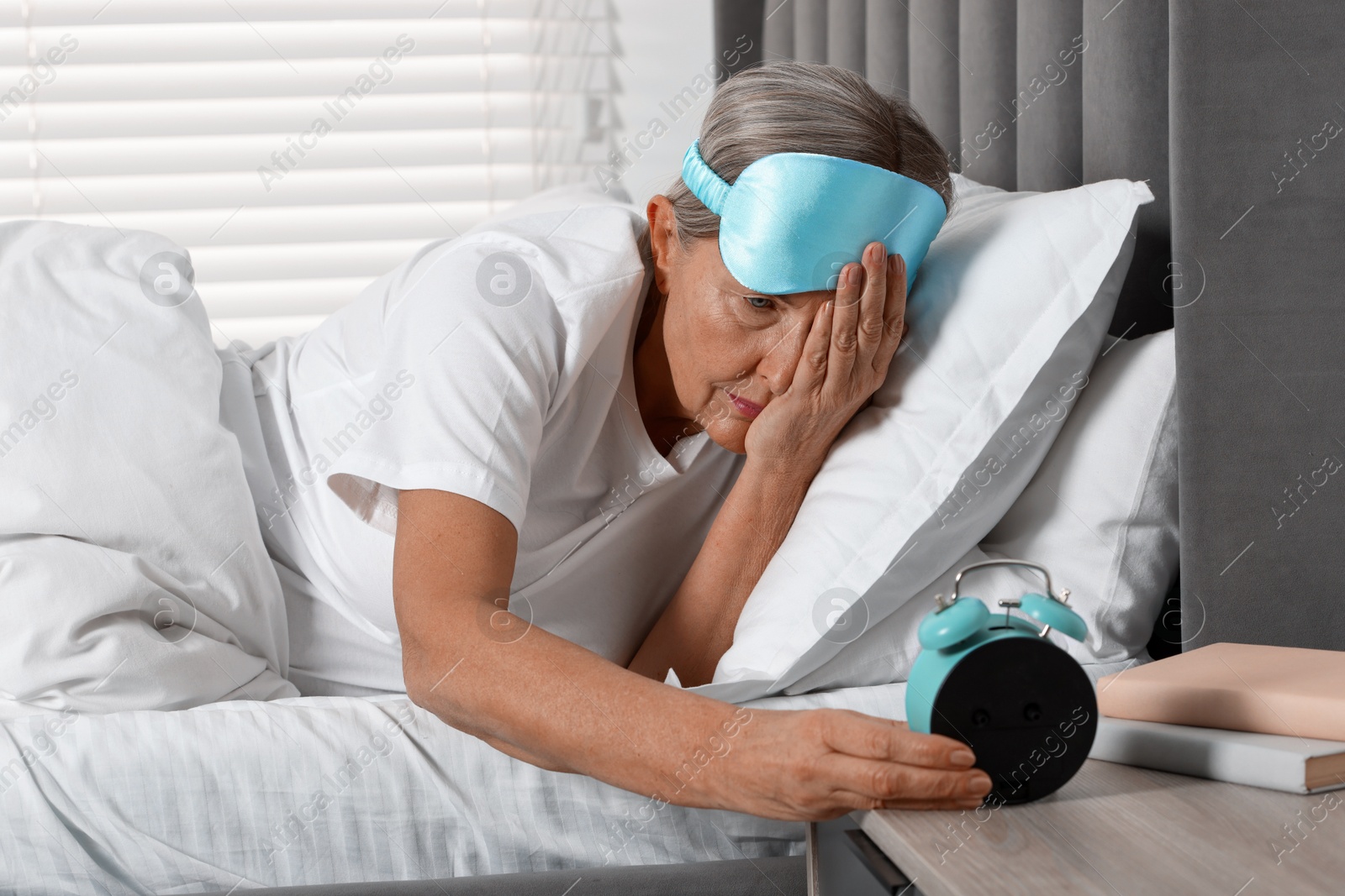 Photo of Overslept woman looking at alarm clock in bed indoors