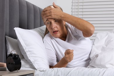 Photo of Overslept woman looking at alarm clock in bed indoors