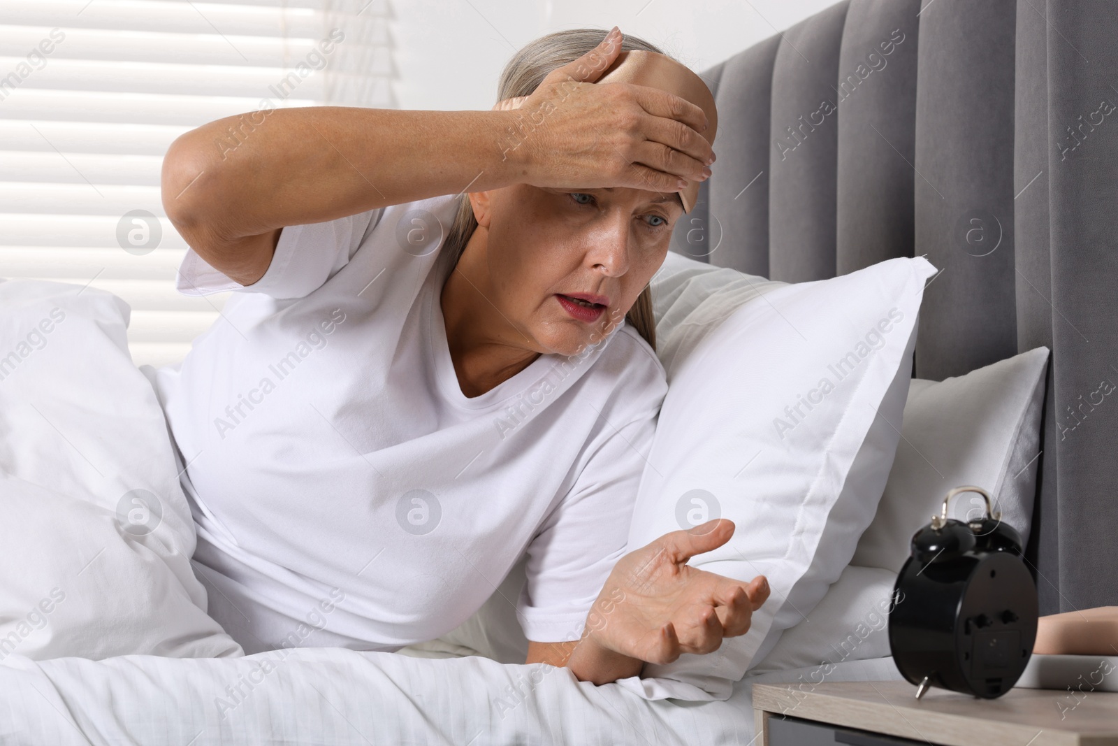 Photo of Overslept woman looking at alarm clock in bed indoors