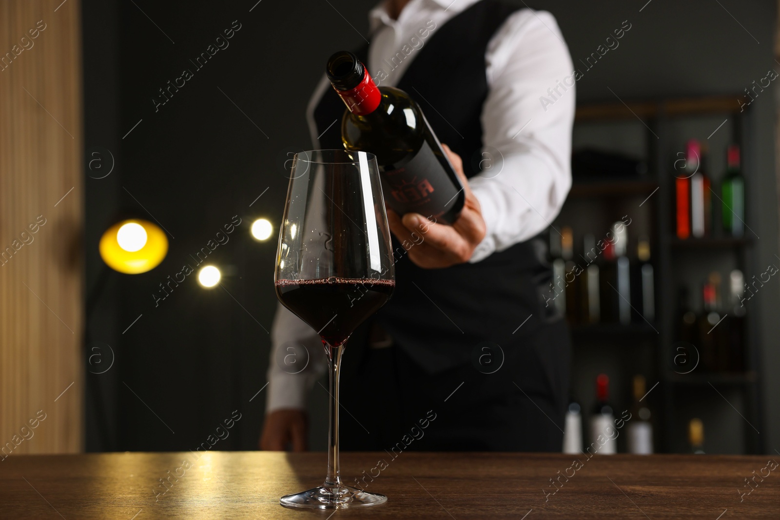 Photo of Professional sommelier pouring red wine into glass at wooden table indoors, closeup