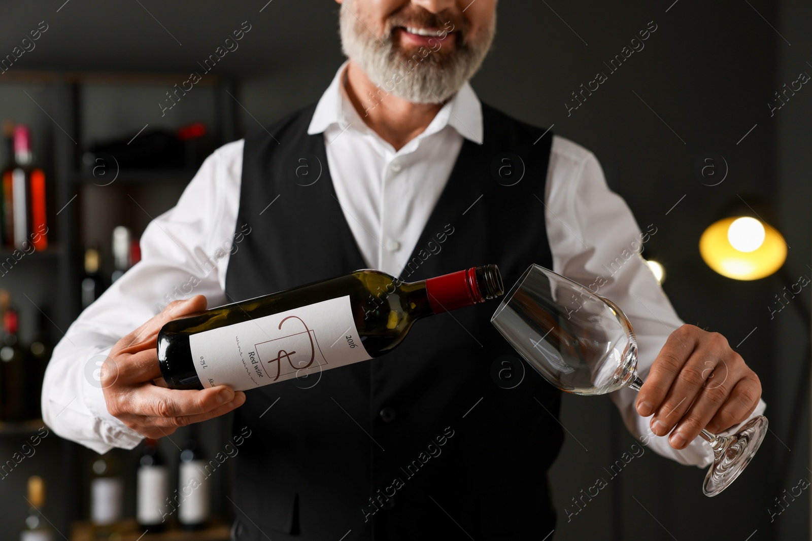 Photo of Professional sommelier pouring red wine into glass indoors, closeup