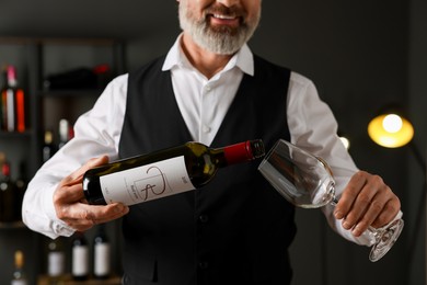 Professional sommelier pouring red wine into glass indoors, closeup