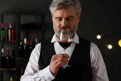 Photo of Professional sommelier tasting red wine in glass indoors