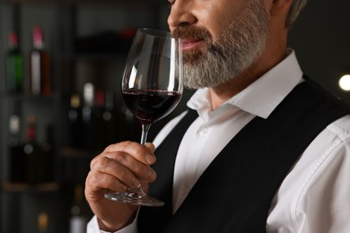 Photo of Professional sommelier tasting red wine indoors, closeup