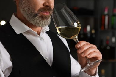 Photo of Professional sommelier tasting white wine in glass indoors, closeup