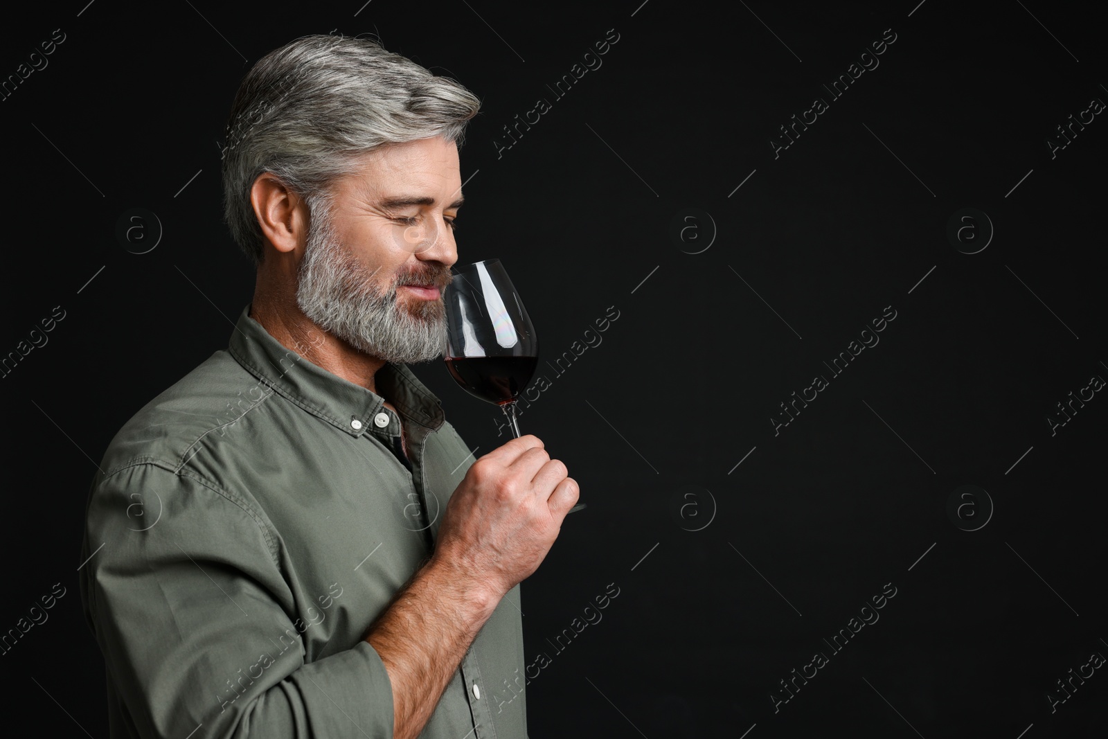 Photo of Professional sommelier tasting red wine on black background, space for text